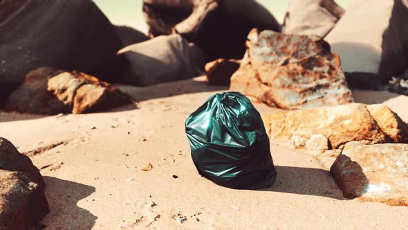 Black Plastic Garbage Bag Full of Trash on the Beach