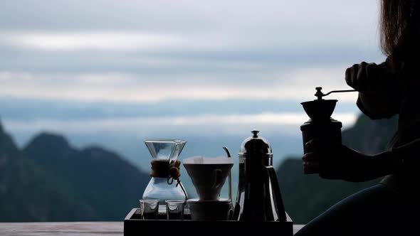 A woman grinding coffee beans with manual stainless steel grinder to make drip coffee