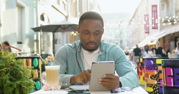 Man in Casual Clothes which Working on Tablet pc while Sitting in Cozy Street Cafe at Time Break