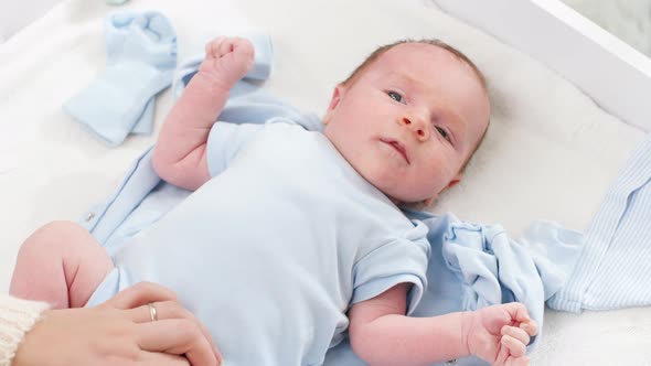 Closeup of Mother Undressing Her Little Newborn Baby Son To Change Clothes on Changing Table at Home