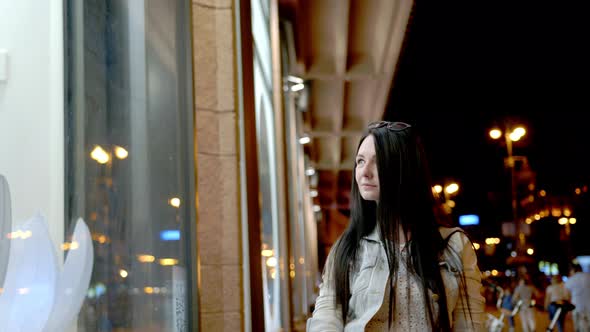 Young beautiful woman in the night city illuminated by lights of shops