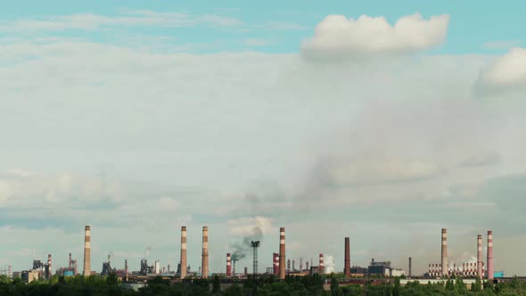 Blue sky with clouds over an industrial plant with smoking chimneys.