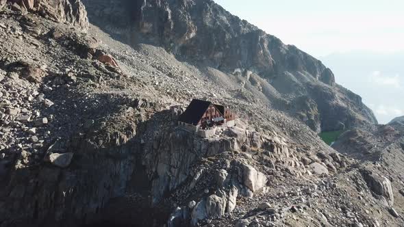 Wooden cabin in the swiss alps, in the middle of high and steep rocky mountains, drone pullback