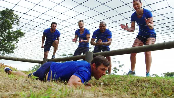 Fit man crawling under the net during obstacle course while fit people cheering 4k
