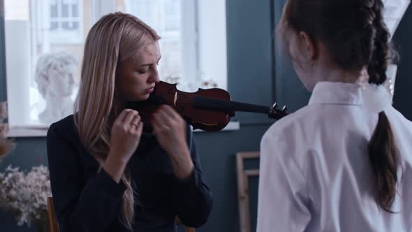 Young Woman Teacher Tuning the Violin in Front of Her Little Girl Student