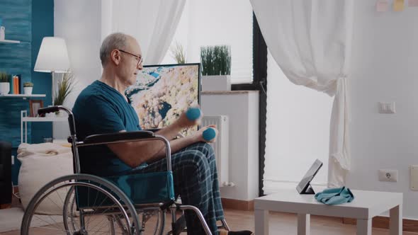 Retired Adult with Disability Lifting Dumbbells and Watching Video