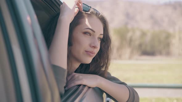 Relaxed Young Lady in Grey Blouse Leans Out of Modern Car