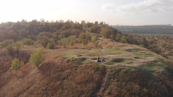 Aerial Top Drone View of Slender Young Mother Do Yoga Exercises with Child Daughter on High Hill in