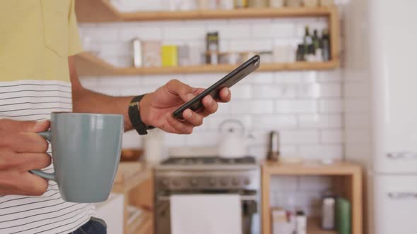 Mid section of man using smartphone while holding a cup of coffee