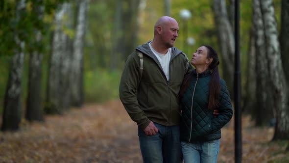 A Middle-aged Couple in Love, a Woman with Dark Hair and a Bald Man Walk Through the Autumn Forest