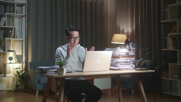 Asian Man Having Video Call On Laptop While Working With Documents At Home