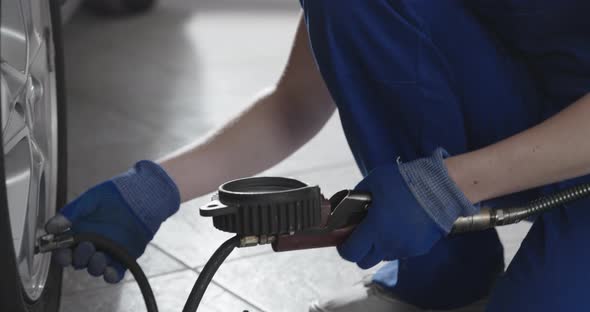 Female mechanic doing a car service in the auto repair shop, she is checking tire pressure