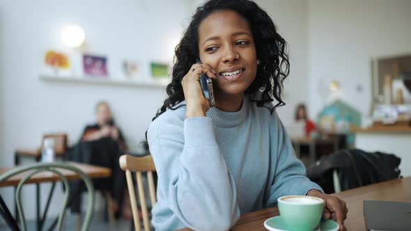 Pleased African woman wearing blue sweater talking on phone