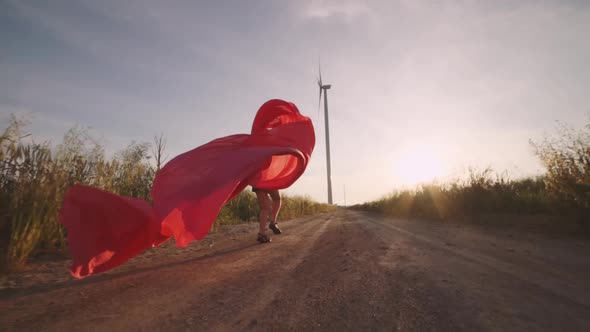 Woman with Pieces of Red Cloth Run to the Wind Generator in the Field