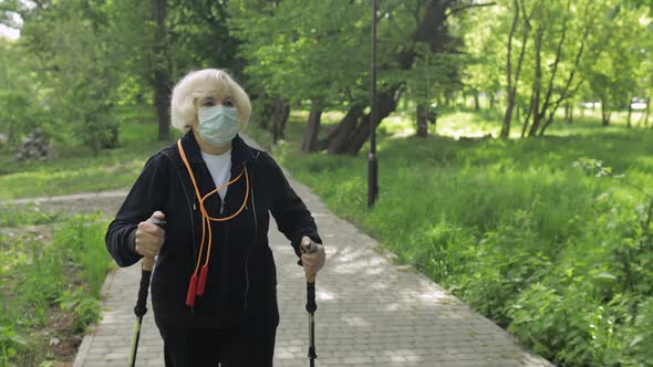 Active Senior Old Woman in Mask Training Nordic Walking in Park at Quarantine