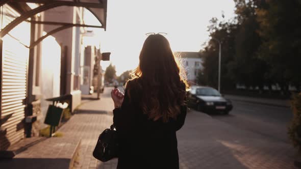 A Sensual Young Girl with Long Hair in Stylish Clothes Goes Along a City Street and Spins with