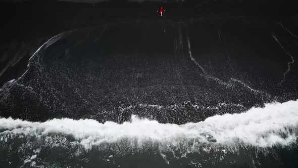 Aerial View of a Girl in a Red Dress Sitting on the Beach with Black Sand. Tenerife, Canary Islands