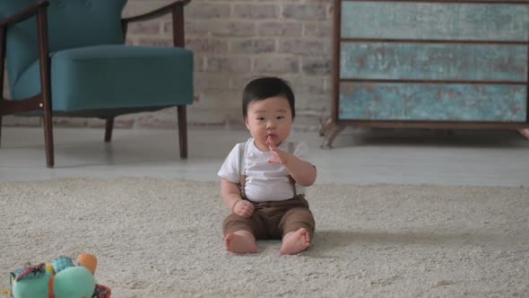 Small Asian boy child sits on the floor in the living room and looks at camera