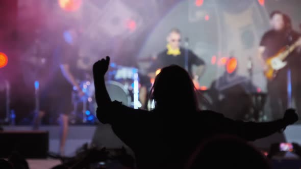 Silhouette of Woman in Crowd at Rock Concert Showing Sign Devil's Horns Gesture