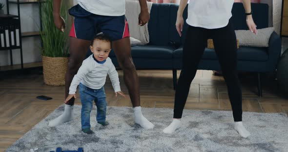 Couple Squating Together During Family Home Workout Near their Playful Cute Little Child