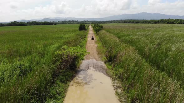 Drone is Flying Behind an ATV Driving on a Dusty Road in Dominican Republic