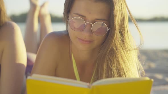 Close-up Portrait of Beautiful Young Woman Reading Book at Sunset on Sandy Beach. Charming Slim