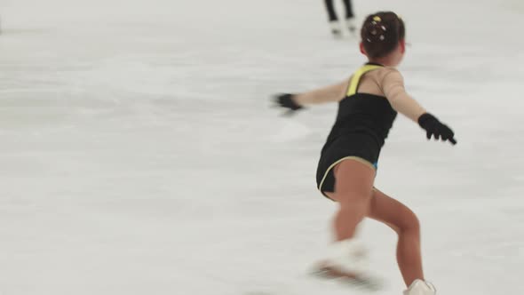 Little Girl Figure Skater in Training Costume Skating and Spinning Around on the Rink