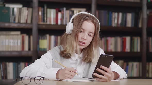 Cute Child Girl Wearing Headphones Studying Online in Mobile App By Video Call with Remote Teacher