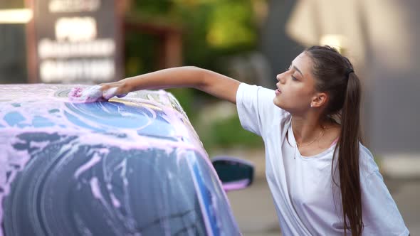 A Young Blonde Woman Washes Her Car