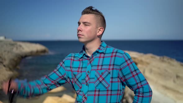 A Young Man Stands on the Background of the Sea, A Man in a Blue Shirt Puts on Sunglasses, Explores