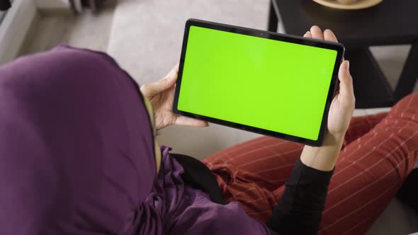 A Muslim Woman Looks at a Tablet (Horizontal) with Green Screen in an Apartment  Top Closeup