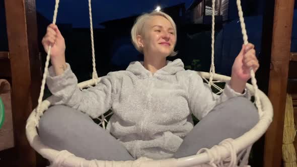 The Girl Swings on a Swing in the Evening and Smiles