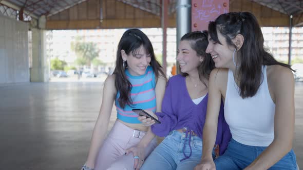 Close View of Three Happy Girls Sitting Looking at Phone and Laughing