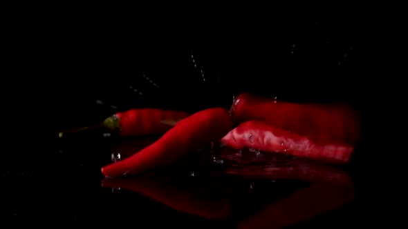 Falling Red Peppers On Wet Surface Against Black Background. Locked Off