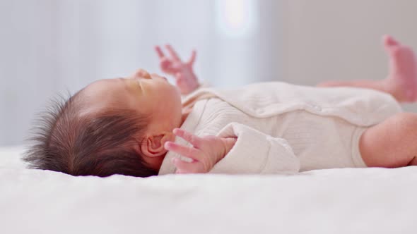 Close up happy newborn baby lying on a white blanket and moving hands and legs