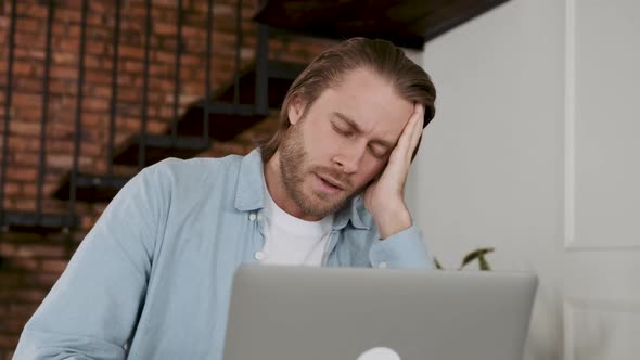 Tired and Sleepy Young Man is Working on His Lap Top in the Living Room