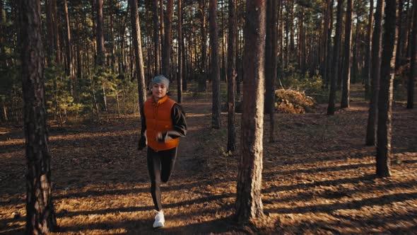 Young Woman Jogging on Trail in Autumn Forest at Sunrise