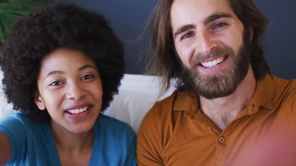 Portrait of mixed race couple blowing kisses on videocall while sitting on the couch at home