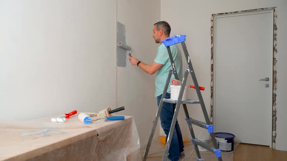 A Man in a Shirt Paints the Walls with a Roller Gray