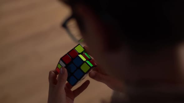 Closeup View From Back of Unrecognizable Smart Child Boy in Eyeglasses Quickly Rotating Rubik Cube