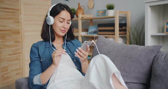 Female Student Enjoying Music Through Headphones Touching Smartphone Screen