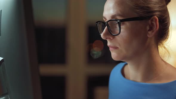 Woman in Glasses Looking on the Monitor and Surfing Internet. The Monitor Screen Is Reflected in the