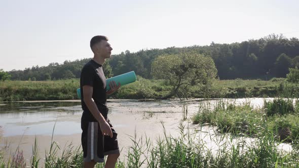 Male walking along river with fitness yoga mat in hands.