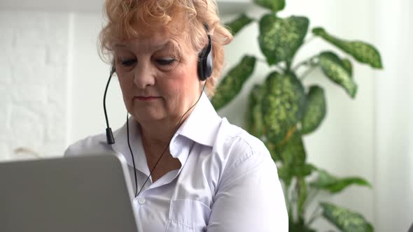 An Elderly Woman Holds a Laptop and Calls