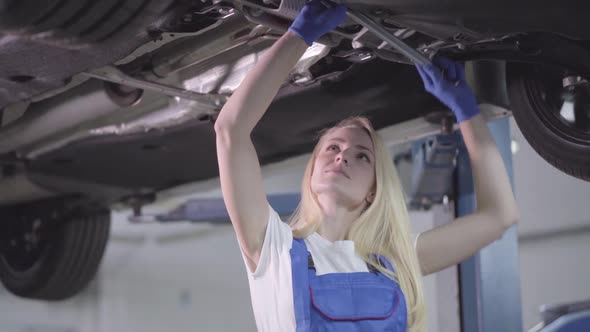 Camera Approaching Slowly To Face of Young Caucasian Woman in Workrobe Standing Under Car 