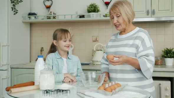 Grandmother and Granddaughter Cooking in Kitchen Breaking Eggs in Bowl Talking