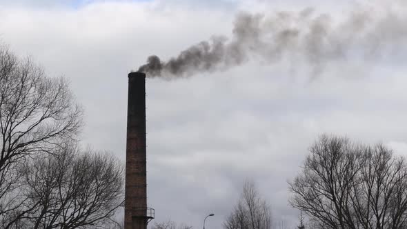 Brick chimney of an old industrial factory emitting dark black smoke into the atmosphere polluting t