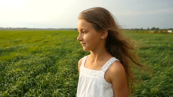 Child, Little Girl Standing in a Green Grassy Field, the Wind Blows Her Hair