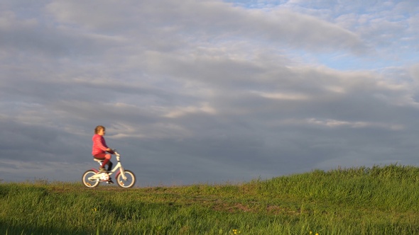 Little girl rides a bicycle rides on a scenic rural road at sunset