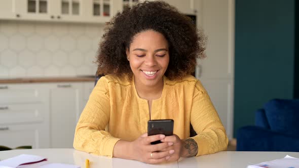 Serene AfricanAmerican Woman Sitting at the Desk at Home and Using Smartphone